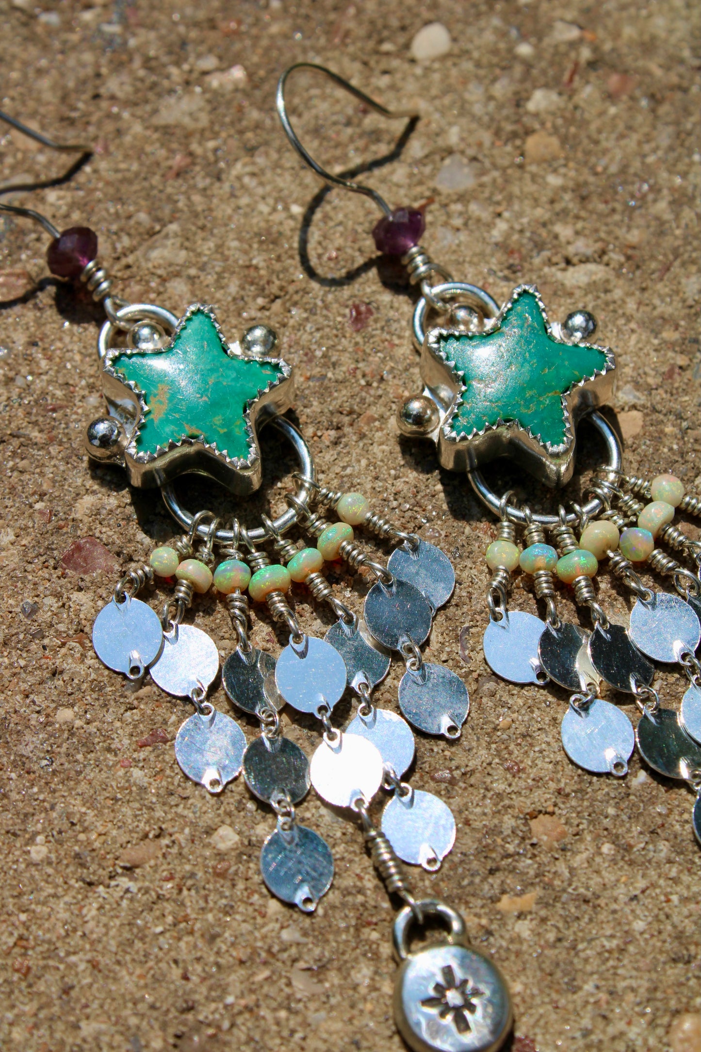 Star-shaped earrings with green stones and silver accents on a sandy background