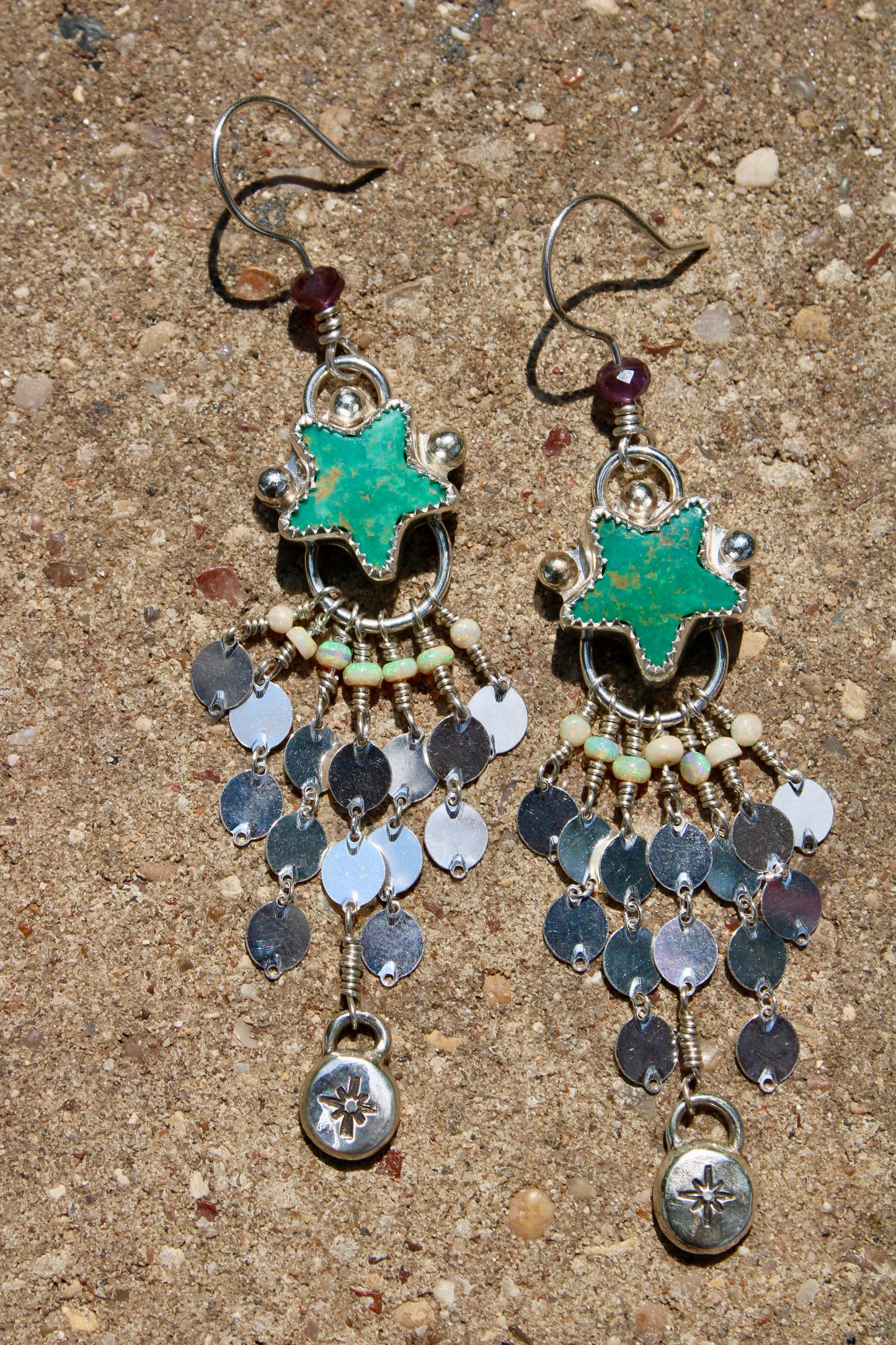 Pair of earrings with star-shaped Turquoise and coin-like pendants on a textured surface.