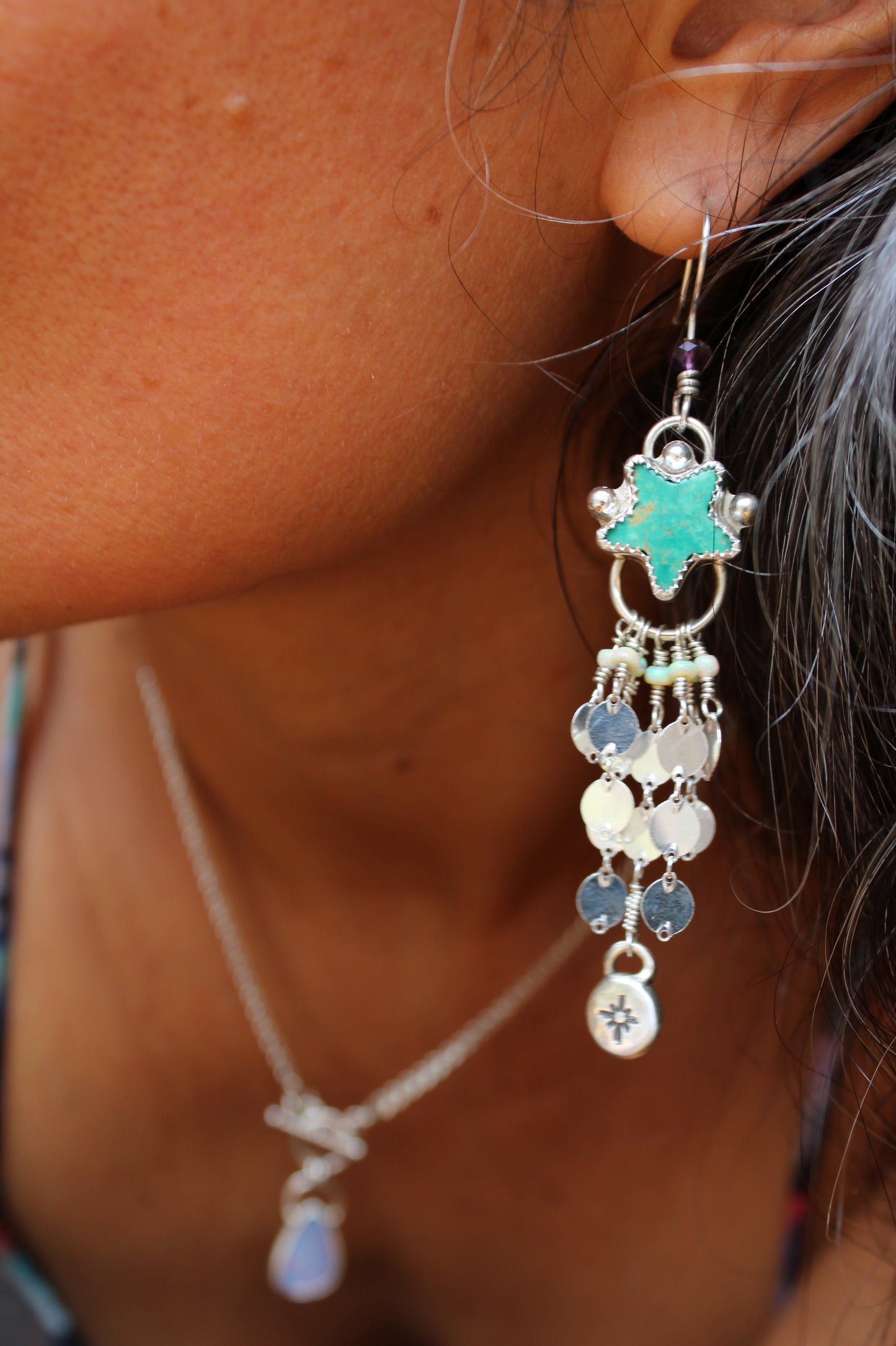 Close-up of a person wearing a detailed earring with a turquoise star and dangling beads.
