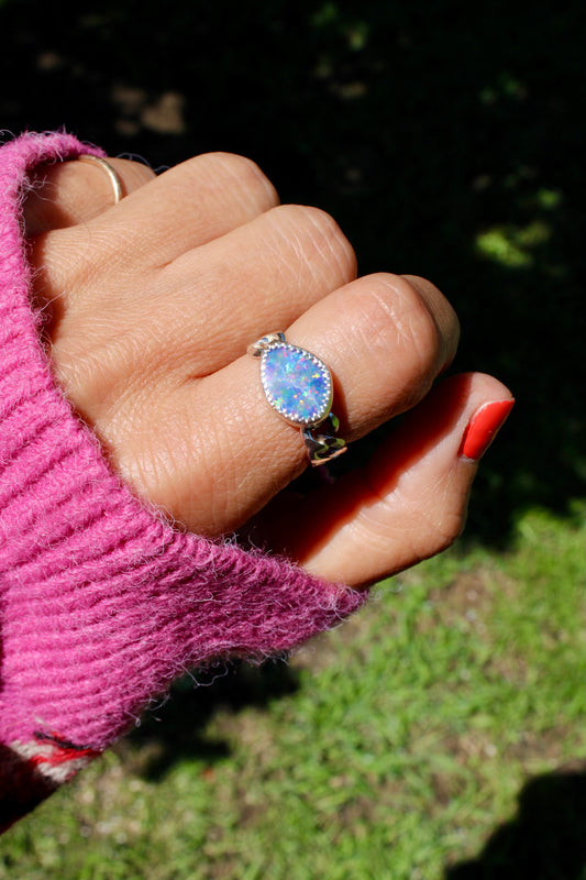 Hand wearing a ring with a blue opal stone against a blurred natural background