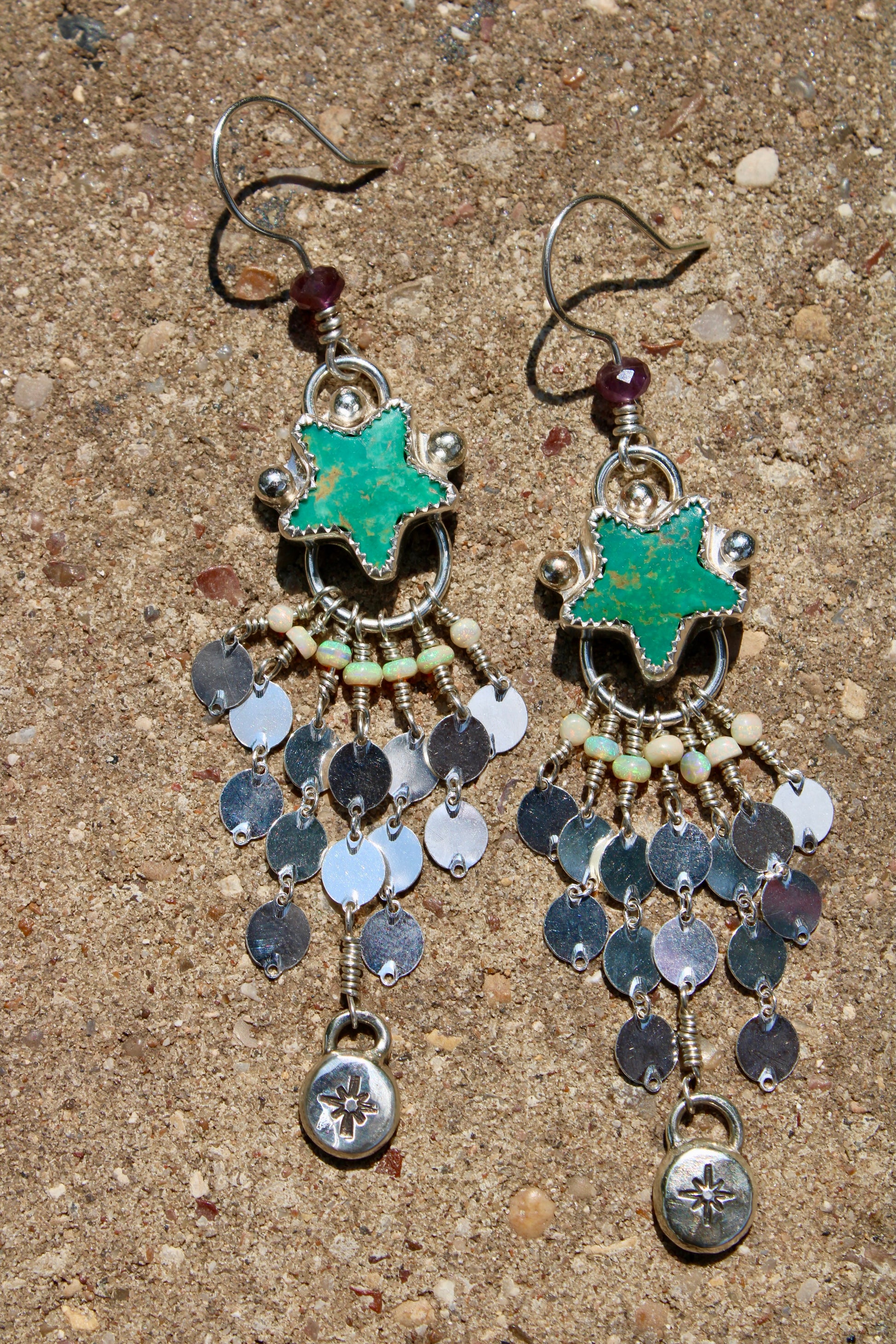 Pair of earrings with star-shaped Turquoise and coin-like pendants on a textured surface.