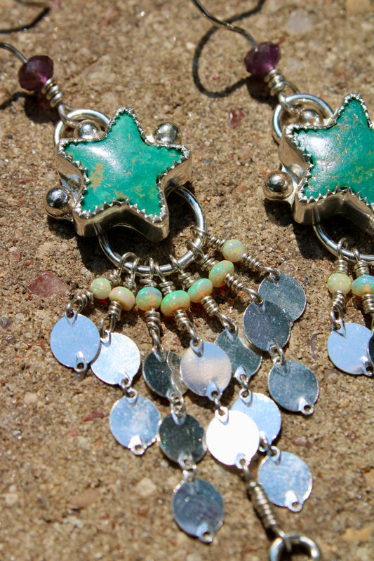 Star-shaped earrings with green stone and metallic chain on a textured surface