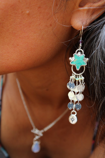 Close-up of a person wearing a detailed earring with a turquoise star and dangling beads.